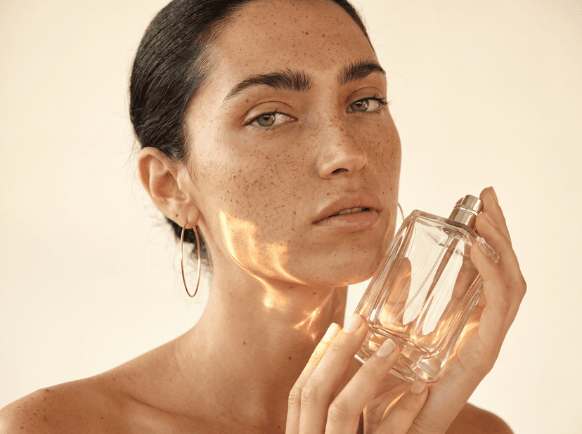 Una modelo sostiene un frasco de perfume de vidrio junto a la mandíbula, con la luz atravesando el cristal